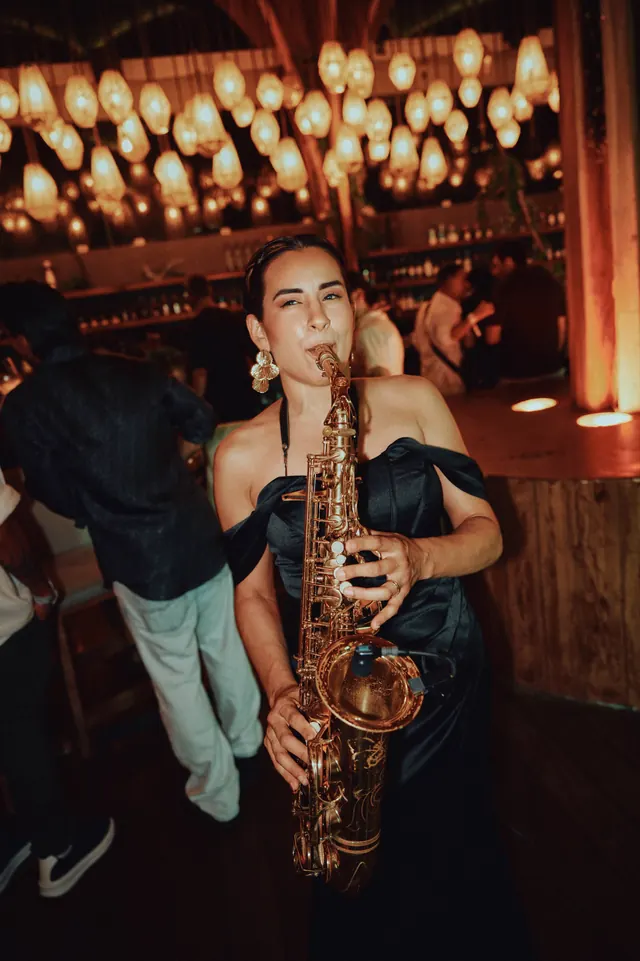 A saxophonist playing under warm hanging lights at the evening event